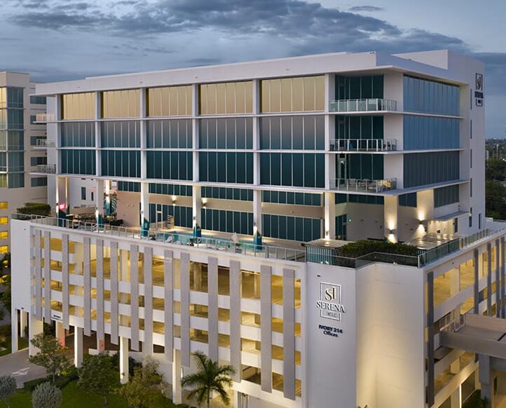 Final architectural hero shot showcasing a professional post-production workflow. The image demonstrates high-end retouching on a modern multi-use building, including vertical integrity, removal of environmental clutter, and luminance range masking to shift focus to the illuminated hotel signage and rooftop pool deck.